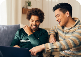 Two people sitting on a sofa smiling at a laptop screen