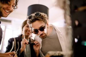  A group of individuals shopping indoors, with one person wearing sunglasses and another holding a pair of glasses, closely examining items in a stylish, well-lit store.