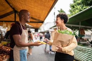 woman paying a small merchant with her phone and seems happy to reap benefits from purchasing with the same business.