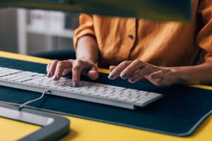 A person focused on typing at a desk, with hands positioned on a keyboard, surrounded by a tidy workspace.