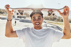 Man smiling and holding a skateboard above his head