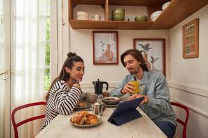 A man and woman are seated at a table, engaged with a tablet in front of them, sharing ideas and collaborating.