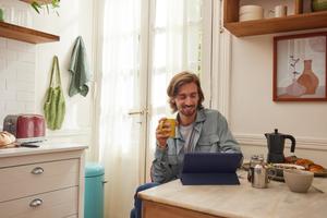 Man drinking coffee at home, browsing on tablet while smiling