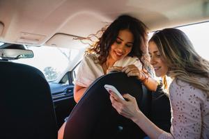 Zwei junge Frauen im Auto schauen aufs Handy.