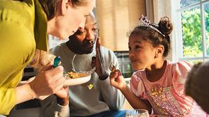 Two parents feeding their daughter a HelloFresh meal. 