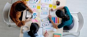 Three people sitting around a table covered with papers illustrating how to connect design with user journey mapping