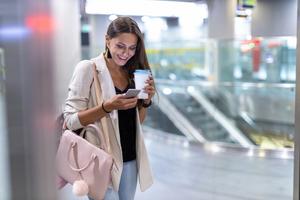 Young woman with smartphone and coffee in the city at night