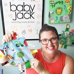 Smiling white woman holding up a Baby Jack & Company Lovey Sensory Blanket in front of company logo