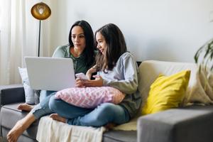 A women and a child sitting on a couch looking at a laptop together