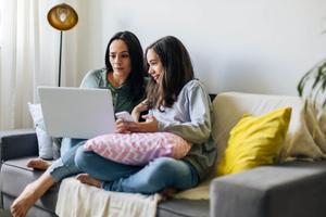 Woman working from home on her laptop with preteen daughter next to her.