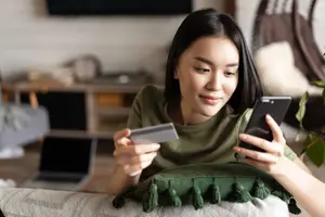 Mujer joven comprando en una tienda online, usando su teléfono y una tarjeta de crédito.