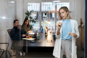 Image looking into a glass conference room with woman writing on glass as two colleagues look on