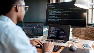 Man sitting in front of two laptops and three screens, coding