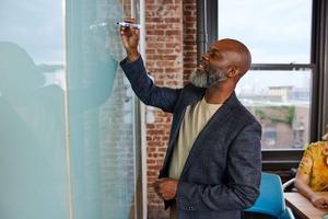 Man wearing a blue blazer writing on a white board with a dry erase board