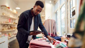 Man holding a point of sale and looking over clothing inventory in a shop