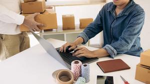 Person holding two boxes in front of another person sitting in front of a computer