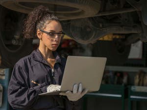 Female employee in autobody shop, working on a laptop
