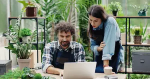 Dos propietarios de floristería trabajando frente un portátil abierto.