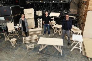 Team of three standing in front of several pieces of wooden office furniture which they have produced.