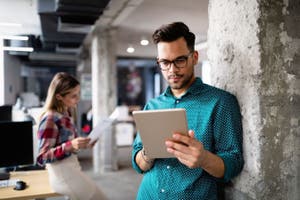 Male coworker using a tablet and female coworker looking at documents, woking in an office together