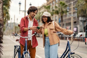 Pareja joven con bicicletas y mochilas que se detiene a mirar juntos su teléfono