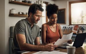 A couple with laptop reviewing paperwork in home kitchen