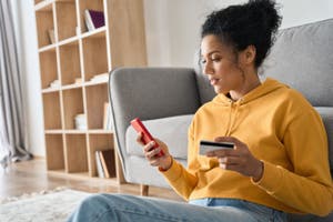 Woman in her living room typing her bank card details into her phone.