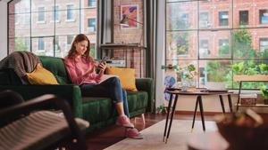 Woman on the couch at home on her mobile device sending automatic transfers.