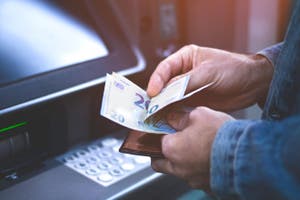 Man standing at an ATM machine with euro notes