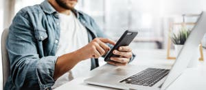 A man tapping on his phone while seated at his desk