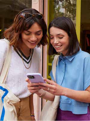 Duas amigas felizes em uma loja olhando para um celular, um exemplo de quando você pode enviar recursos com o PayPal.