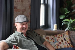 A smiling man sits on a couch in a production studio.