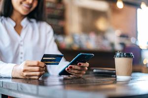 A woman looks at her flat-rate cash back credit card while making a purchase on her phone.