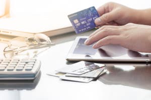 Mann nutzt sein digitales Tablet, während er eine Kreditkarte in der Hand hält, mit der Absicht, online sich über die Kreditline zu informieren.