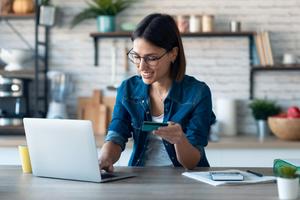 Junge Frau hält eine Debitkarte in der Hand, um online am Computer einzukaufen.