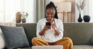 Eine glückliche Frau mit Telefon auf dem Sofa setzt sich neue Sparziele auf und macht Mobiles-Banking.