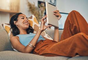 Frau liegt auf Sofa und tippt auf Tablet