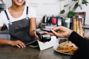 Eine junge Frau bezahlt kontaktlos mit Smartphone im Kaffee und eine  Aufrundungszahlung verwendet.