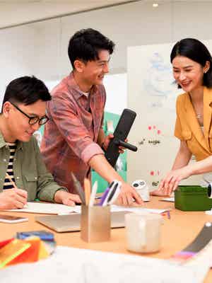 3 business young people working together. Two of them are selecting something from a paper and other is writing on a paper.