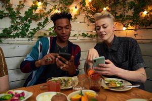 A pair of young people sitting at a table, focused on their smartphones.