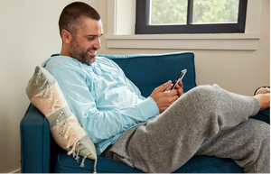 A man relaxing on a couch with his feet up, holding a phone in his hand.