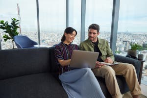 A man and a woman seated on a couch, focused on a laptop.