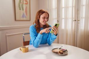 A woman at a table, enjoying a cup of coffee while using her phone.