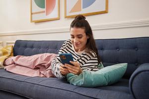 A woman relaxes on a couch, focused on her phone.