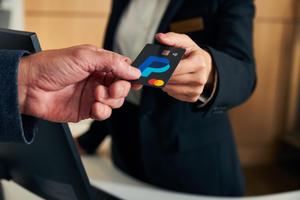 A person presents a credit card while seated at a computer, representing the concept of e-commerce or online financial services.