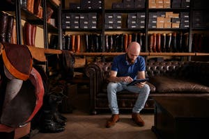 A man seated on a couch inside a leather store, surrounded by various leather goods and furnishings.