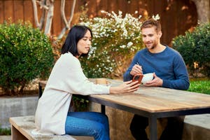 A man and woman sitting at a table, enjoying a cup of coffee together while looking at a mobile phone.