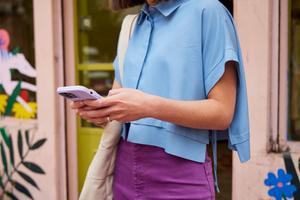 A woman wearing a blue shirt and purple skirt focuses on her phone, indicating engagement with her device.