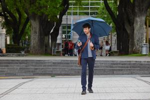 A man holding an umbrella gazes at his phone, appearing engaged despite the rainy weather.