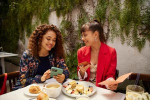 Two women enjoying a meal together at a table, surrounded by food and drinks.